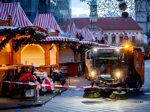 Der Magdeburger Weihnachtsmakrt mit geschlossenen Ständen. Ein Reingungsfahrzeug putzt davor die Straße. Im Hintergrund zeichnen sich Teile der Johanniskirche ab.