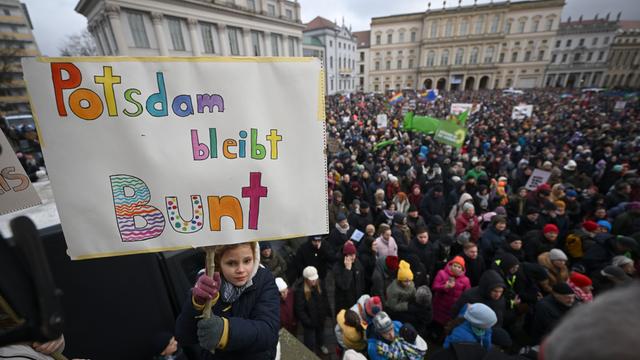 Eine Menschenmenge hat sich auf einem Platz versammelt. Ein Mädchen hält ein Schild in die Höhe. Darauf steht "Potsdam bleibt Bunt". 