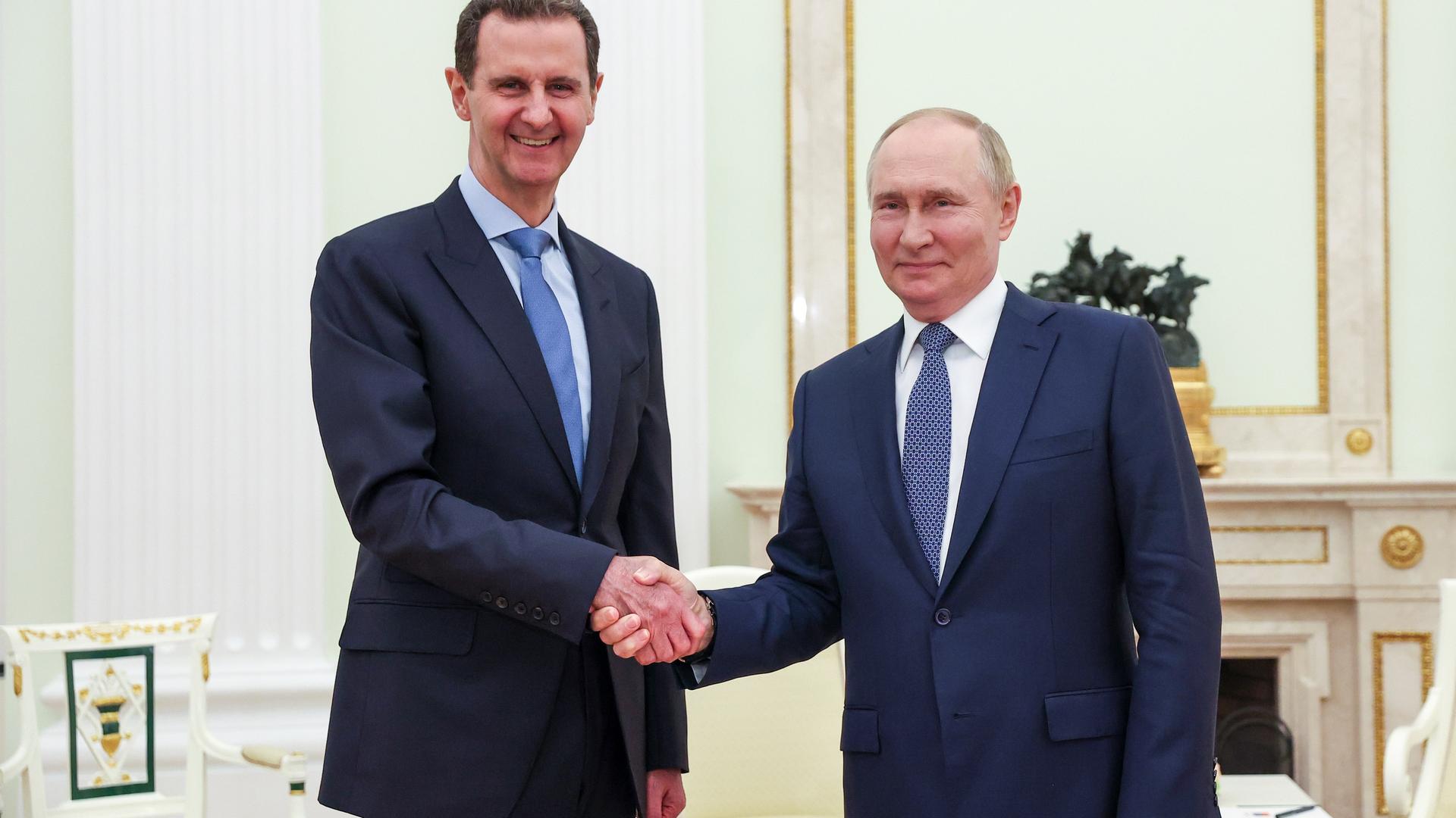 Wladimir Putin und Bashar al-Assad schütteln sich die Hände und lächeln in die Kamera.