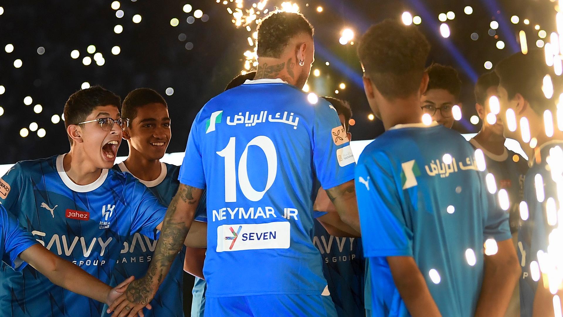 Brasiliens Superstar Neymar Jr. im Trikot seines neuen Vereins Saudi Al Hilal wird von mehreren Jungen abgeklatscht, als er das Stadion betritt, es ist dunkel.