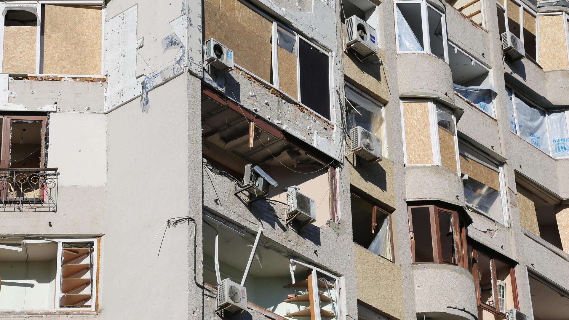 Die Fenster und Balkone eines Wohnhauses wurden mit Brettern verschlagen. Viele Fenster sind zerbrochen, vermutlich aufgrund von Druckwellen von Explosionen.