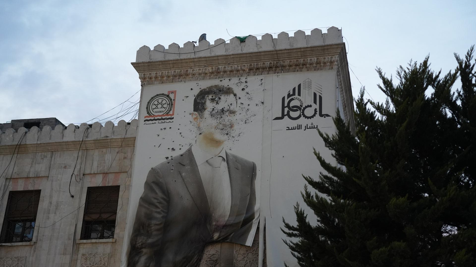 An einem Haus ein Bild von Assad, man sieht deutlich Kampfspuren und Einschusslöcher.