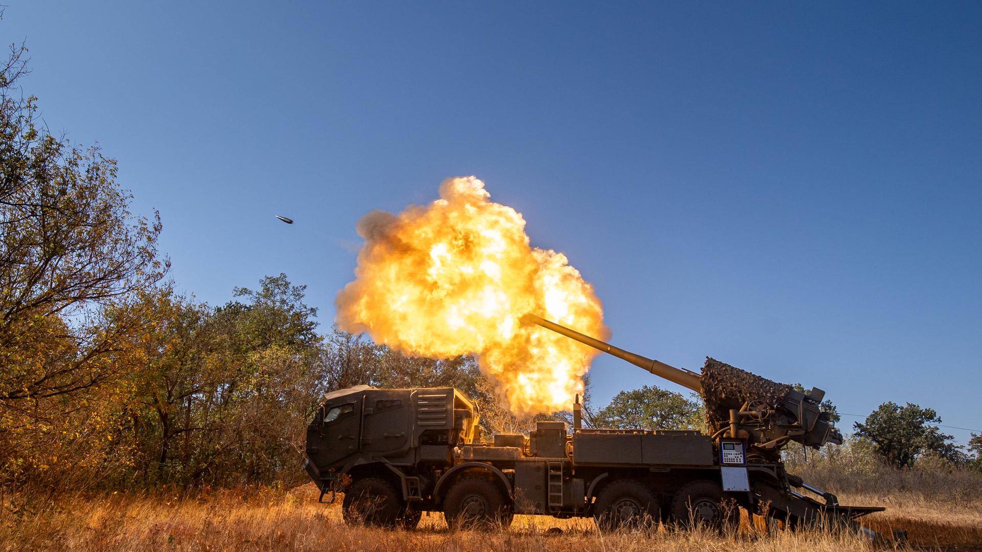 Ein Geschütz feuert. Die Explosion und das Geschoss sind zu sehen. Die Umgebung ist erleuchtet.