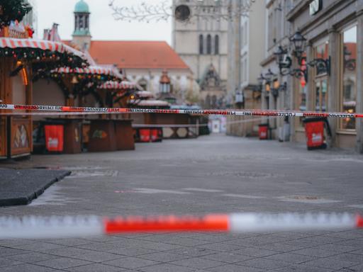 Eine Polizeiabsprerrung mit zwei rot-weißen Bändern vor geschlossenen Ständen auf dem Magdeburger Weihnachtsmarkt. Im Hintergrund zeichen sich Teile der Johanniskirche ab.