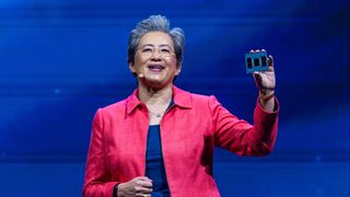 Lisa Su, CEO at AMD, holding up an AI processor on the keynote stage of a tech conference. Decorative: Su has been photographed with a telephoto lens, is wearing a pink jacket, and is stood against a blue background.