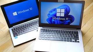 Windows 10 and Windows 11 logos pictured on laptop screens sitting side-by-side on a desk.