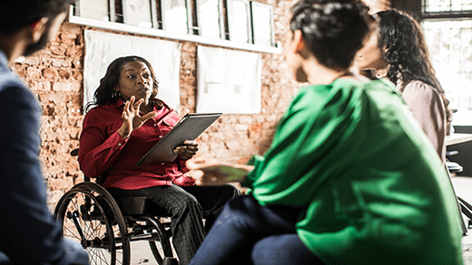 Wanita di kursi roda sedang memimpin rapat dengan tiga orang rekannya dalam suasana kantor yang santai