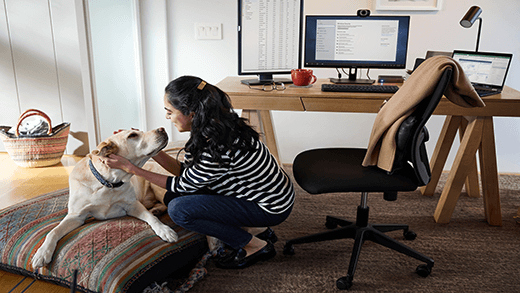 Kvinna som knäar för att klappa sin hund på ett hemmakontor med skrivbord, dator och stol