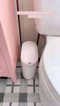 a white toilet sitting in a bathroom next to a pink cabinet and trash can on the floor