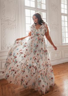 a woman in a white dress standing on a wooden floor next to a large window