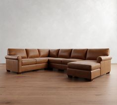 a brown leather sectional sofa sitting on top of a hard wood floor next to a white wall