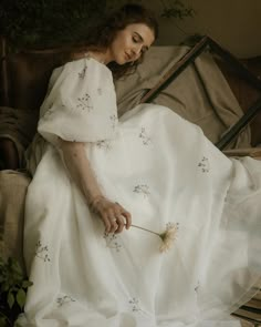 a woman in a white dress sitting on a chair with a flower in her hand