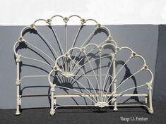 a white metal bed frame with intricate designs on the headboard and foot board, in front of a gray wall