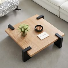 a coffee table with two black legs and a bowl of nuts on the top, in front of a white couch