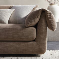 a couch with several pillows on it in front of a vase filled with dried flowers