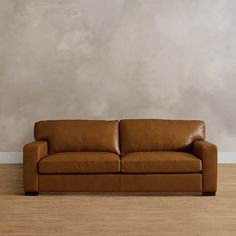 a brown leather couch sitting in front of a wall with a wooden floor and white walls