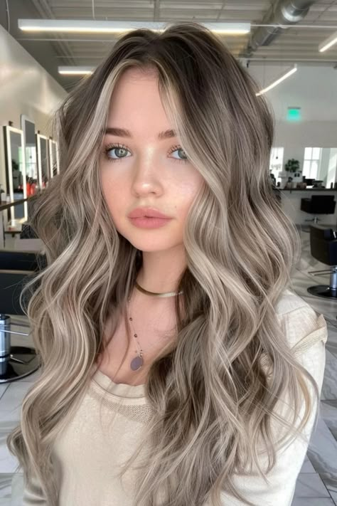 Woman with long, wavy blonde hair in a modern salon setting. Light Brown With Ash Blonde Highlights, Dark Blonde With Shadow Root, 2025 Trend Hair Color, Brunette With Ash Highlights, Ash Brown Toner Formula, Silver Platinum Blonde Hair, Brown Shadow Root To Blonde, Ash Blonde Highlights On Dark Brown Hair, Unique Natural Hair Color Ideas