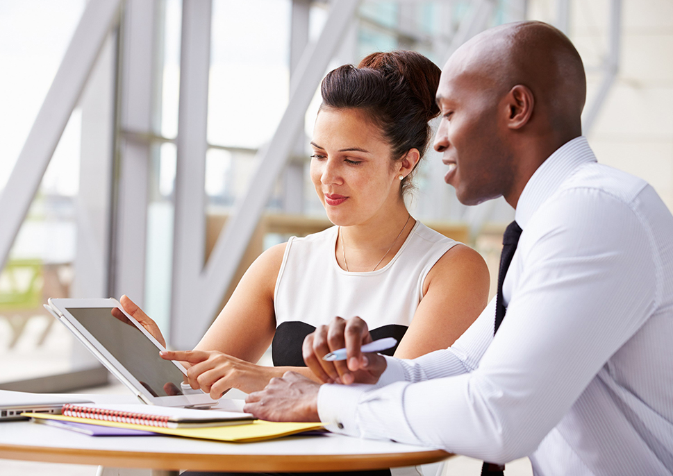 Two professionals in a brightly lit office pointing at a tablet