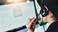 Woman in front of computer with headset on.