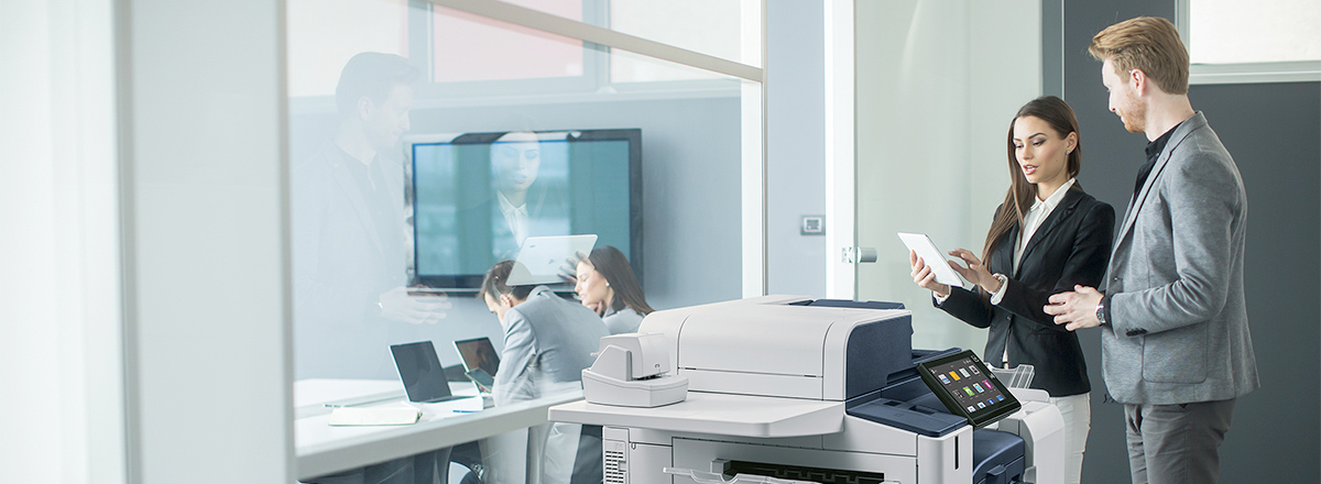 Co-workers looking at a tablet, next to an AltaLink B8100 Series MFP