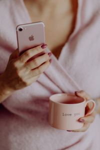 Kaboompics - A woman in a pink sweater holds a pink iPhone and a pink cup in her hands