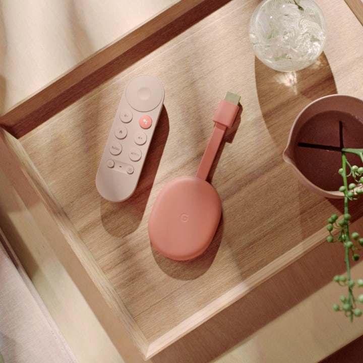 Chromecast with Google TV in Sunrise on a smooth wooden surface next to a plant and a glass art piece