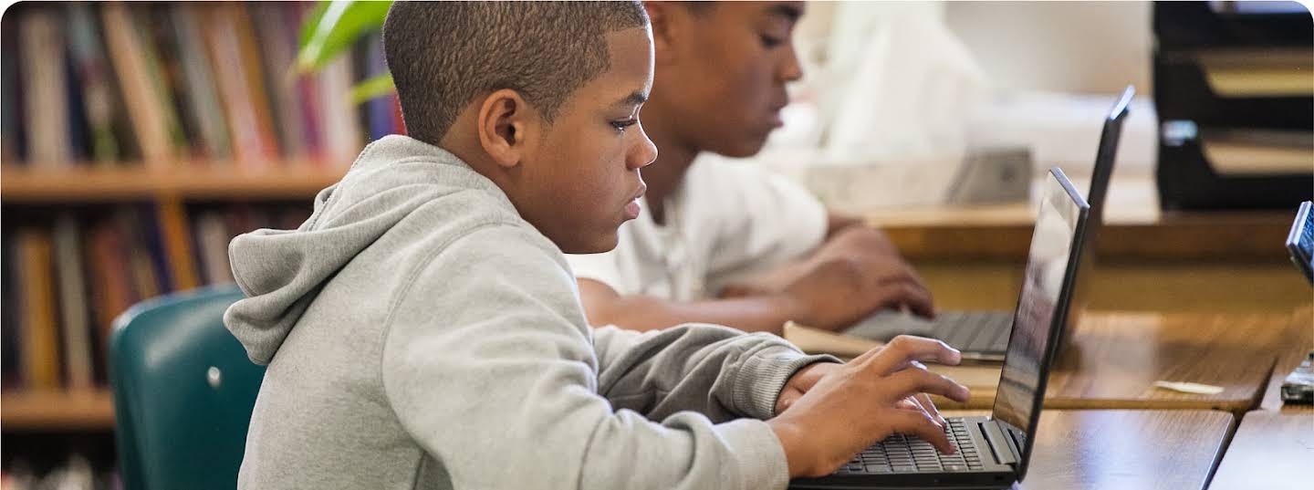 Two students work on Chromebooks at their desks.