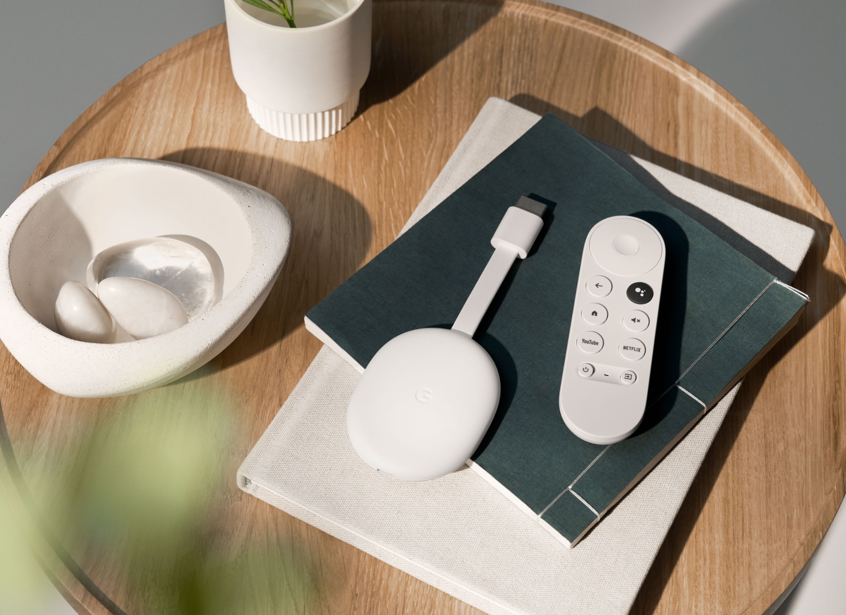 Chromecast with Google TV in Snow on a a pile of journals next to white ceramic pieces