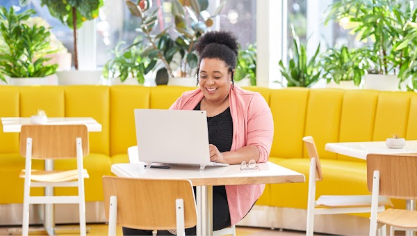 A woman uses her laptop as she sits in a bright yellow cafe space