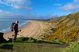 A hiker stands against a long sandy beach stretching to the horizon.