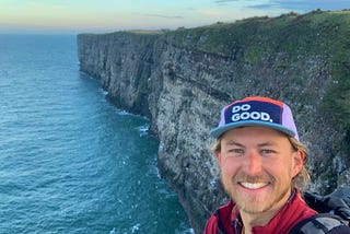 A hiker smiles happy with sea cliffs in the background.