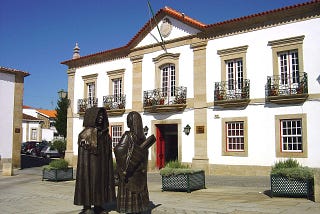 Two bronze statues in traditional attire stare at each other in the main square of Miranda do Douro.