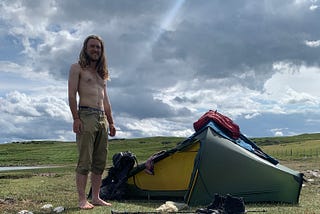 A hairy topless hiker shows ribs and abs beside his tent.