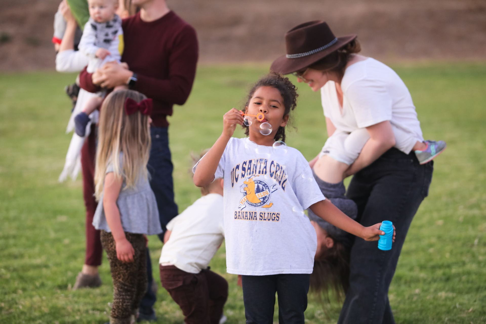 Children playing outside with bubbles next to two adults  