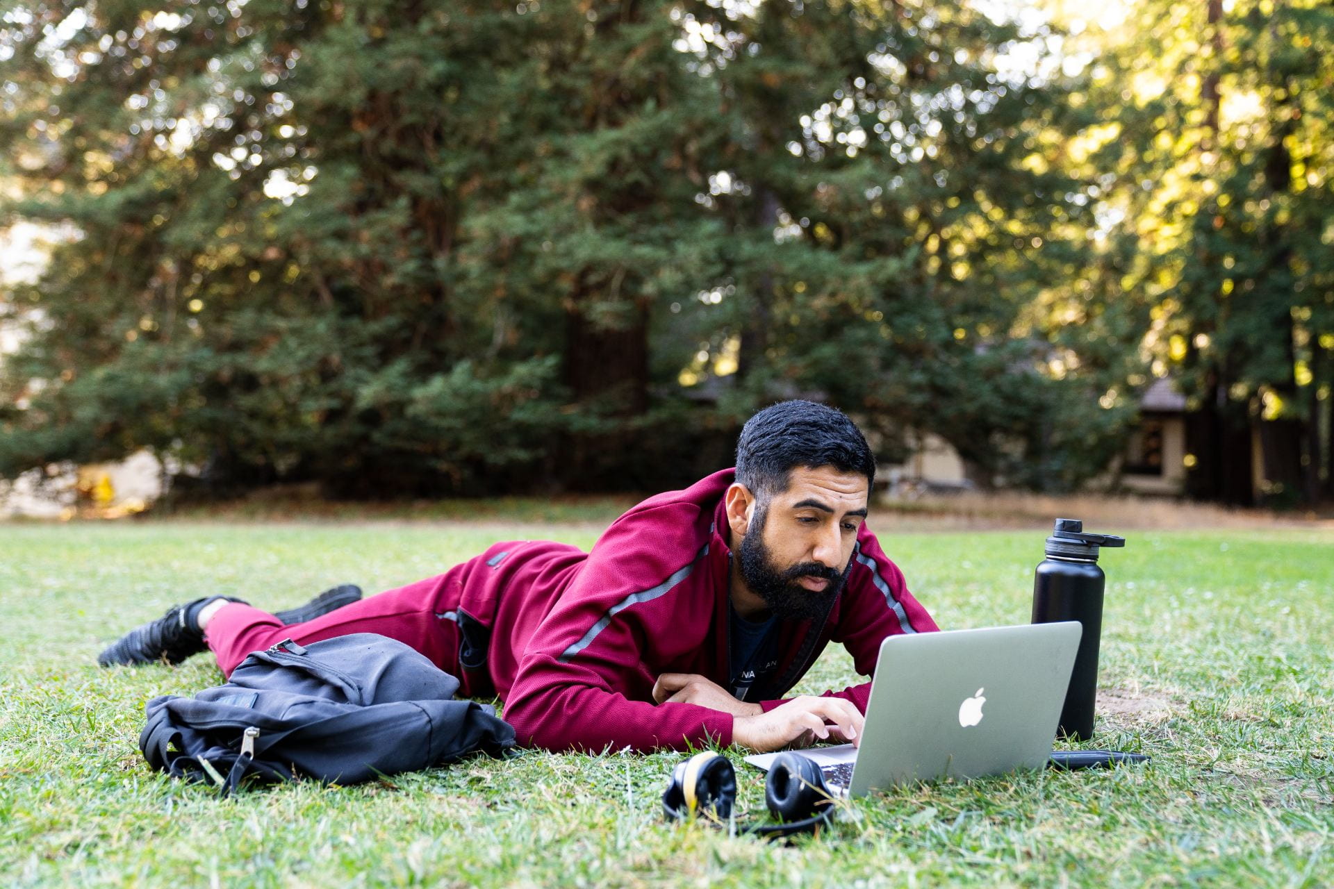 A student laying in the grass looking at a computer.