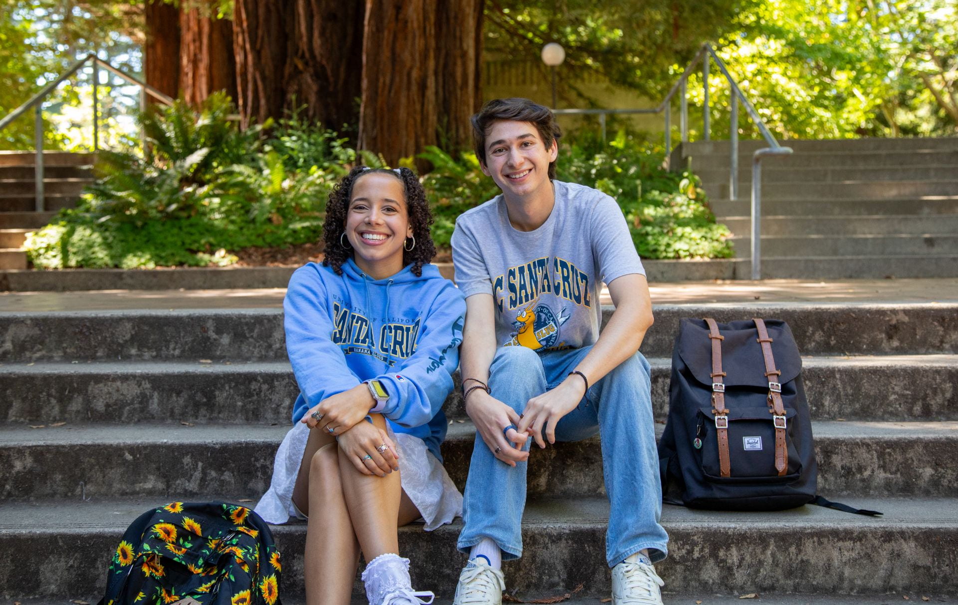 Two students wearing UCSC shirts smiling and sitting on stairs