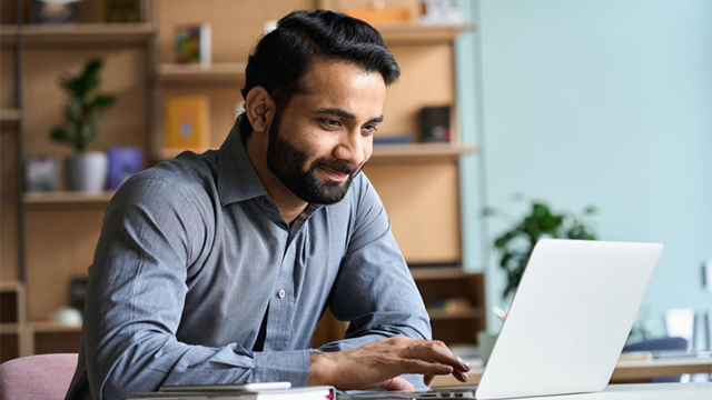 Person sits a desk looking at laptop and smiling