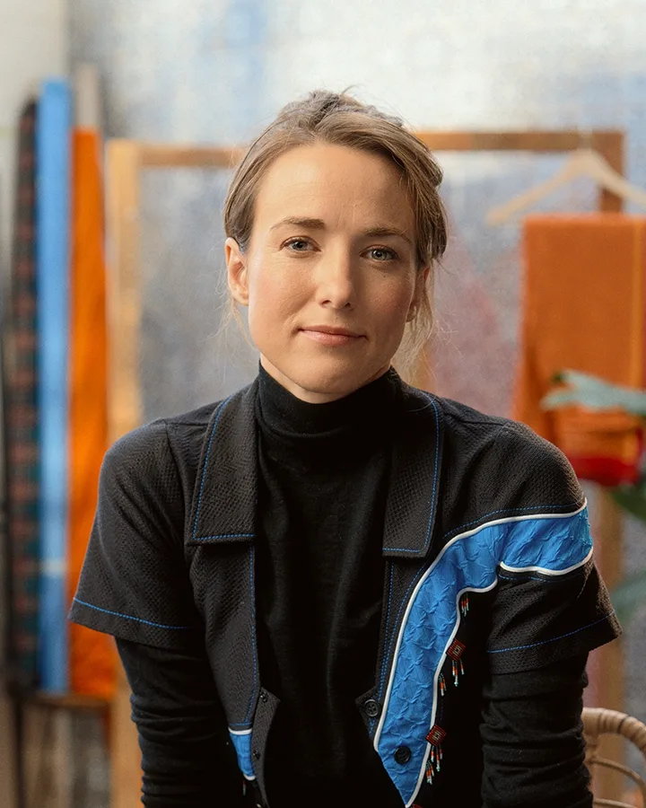 A woman sitting on a chair in front of colorful fabric.