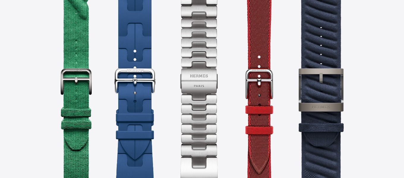 Front view of five Hermès watch bands showing a Rouge Grenat (red) Torsade, a Vert Moyen (green) Kilim, a Satiné (satin silver) Grand H, a Rouge Grenat/Vermillion (red with red trim) Attelage Twill Jump Single Tour, and a Bleu Nuit (blue) En Mer.