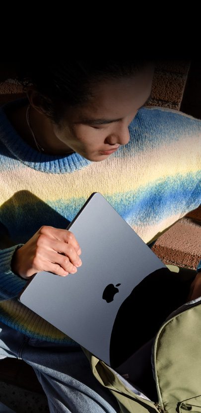 A person sliding a 15-inch Midnight MacBook Air into a backpack.