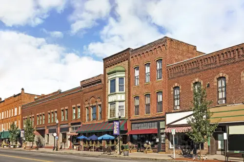 A photo of a typical small town main street in the United States of America. Features old brick buildings with specialty shops and restaurants. Decorated with autumn decor.