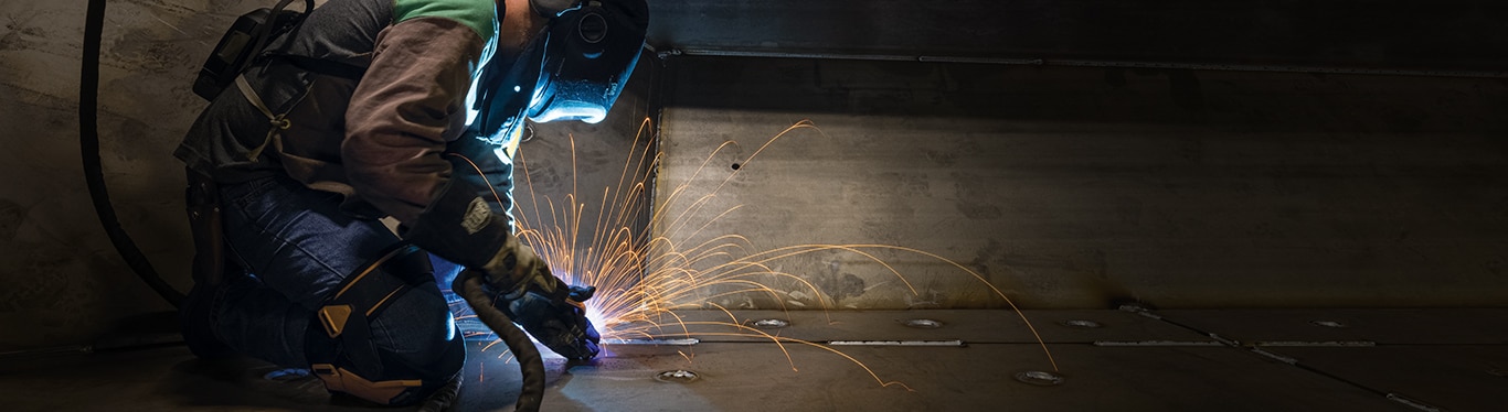 A person in welding suit welding a piece of equipment with sparks flying