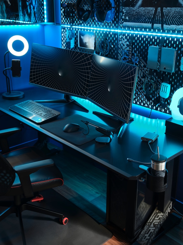 A black UPPSPEL gaming desk with two monitors, a ring light and keyboard on top and a pegboard holding gear behind it.