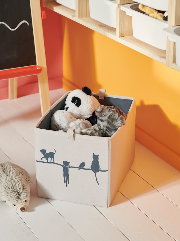 A beige BRANDRÖM box on a floor filled with soft toys including a LILLEPLUT soft toy cat and SKOGSDUVA owl soft toy puppet.