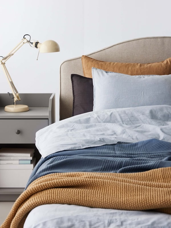 A bed made with blue striped bedding and a tan pillow and blanket.