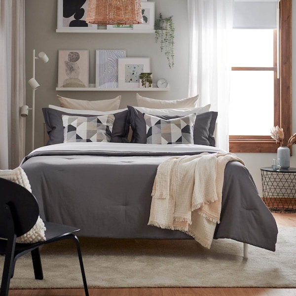 A gray comforter on a be with a beige blanket lying on the edge.