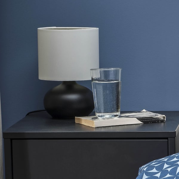 A small black base table lamp with a white shade sitting on a nightstand.