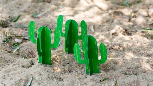 drei Kakteen aus Papier stehen im Sand